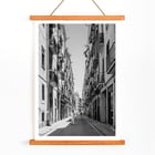 Schwarzweißfotografie von Street of Barcelona, die einen Mann zeigt, der eine schmale Stadtstraße entlanggeht. Schwarzweißposter mit der Abbildung einer schmalen Straße in Barcelona mit dem Titel „Straße von Barcelona“ und einer Person in der Mitte.