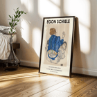 Egon Schiele exhibition poster featuring Woman Seated Back artwork Poster of Woman Seated Back artwork by Egon Schiele showing a woman with a colorful garment sitting with her back turned