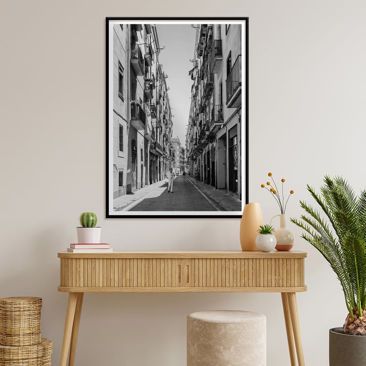 Schwarzweißfotografie von Street of Barcelona, die einen Mann zeigt, der eine schmale Stadtstraße entlanggeht. Schwarzweißposter mit der Abbildung einer schmalen Straße in Barcelona mit dem Titel „Straße von Barcelona“ und einer Person in der Mitte.