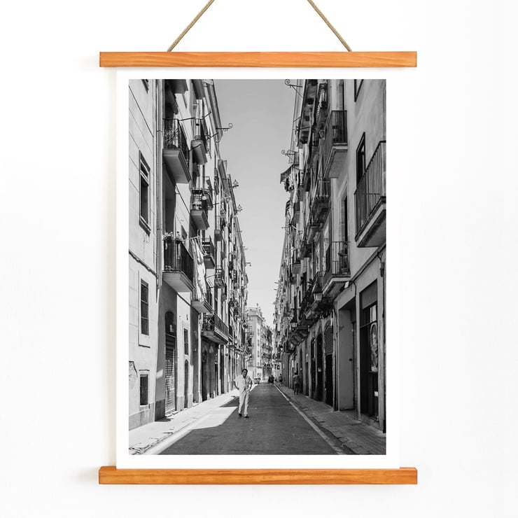 Schwarzweißfotografie von Street of Barcelona, die einen Mann zeigt, der eine schmale Stadtstraße entlanggeht. Schwarzweißposter mit der Abbildung einer schmalen Straße in Barcelona mit dem Titel „Straße von Barcelona“ und einer Person in der Mitte.