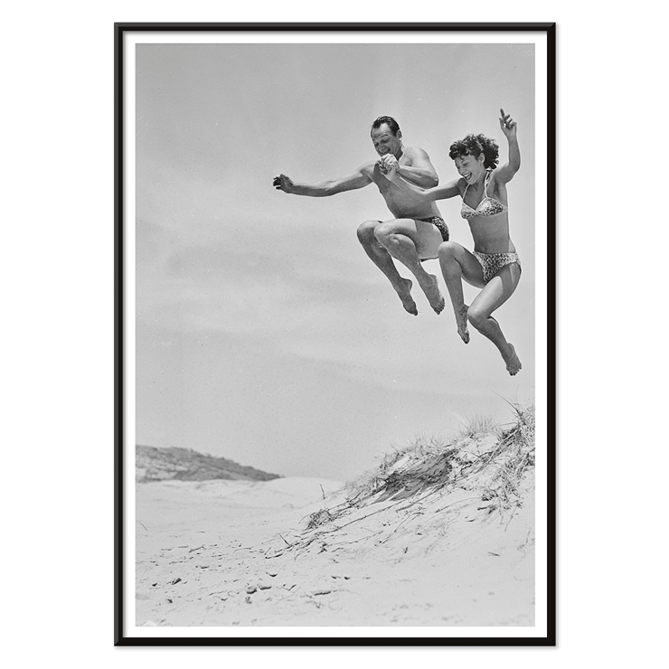 Acrobatic jump at the beach by Tivoli stars Acrobatics at the Beach Poster of Acrobatics at the Beach by Two Tivoli Stars featuring two people in swimsuits jumping on a sandy beach.