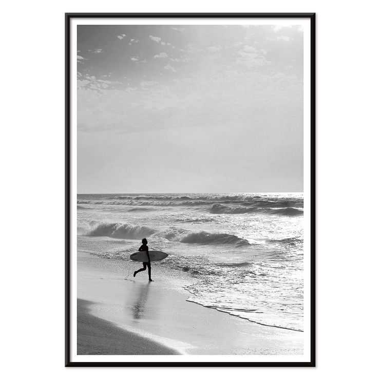 Surfer with a board by the ocean in a black and white picture titled Surfer in Portugal by artist Black Black and white poster Surfer in Portugal by Black & White Picture depicts a lone surfer entering the ocean carrying a surfboard.