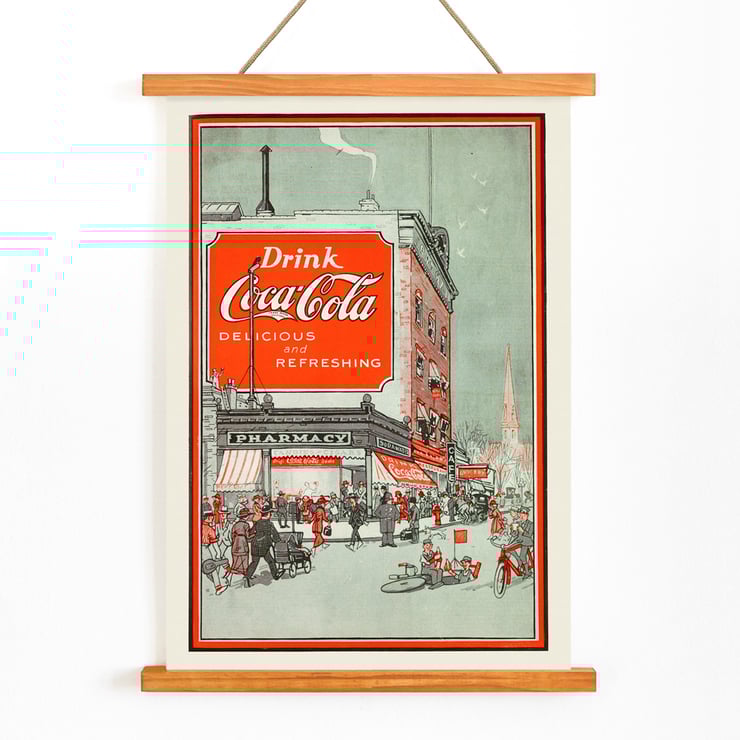Drink Coca Cola vintage advertisement depicting a busy street scene Poster titled Drink Coca Cola showing a bustling street scene with people near a pharmacy and a large Coca Cola billboard