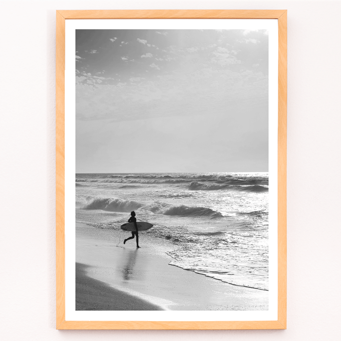 L'affiche noir et blanc Surfer in Portugal de Black & White Picture représente un surfeur solitaire entrant dans l'océan portant une planche de surf.