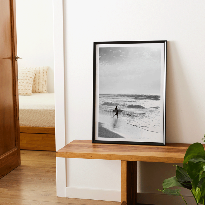 Black and white poster Surfer in Portugal by Black & White Picture depicts a lone surfer entering the ocean carrying a surfboard.