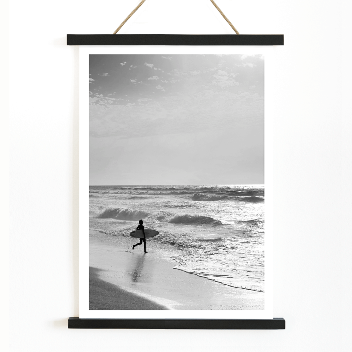 L'affiche noir et blanc Surfer in Portugal de Black & White Picture représente un surfeur solitaire entrant dans l'océan portant une planche de surf.