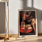 Affiche vintage Cordial Campari de Nizzoli représentant une femme assise avec un magazine et une bouteille sur une table.