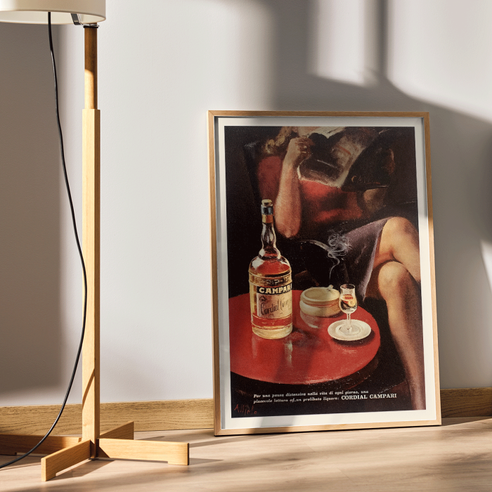 Póster vintage Cordial Campari de Nizzoli que muestra una mujer sentada con una revista y una botella sobre una mesa.